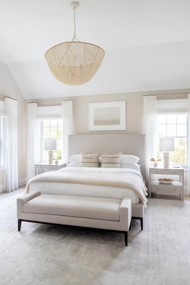 A pale bed and slim upholstered bench sit between bright windows