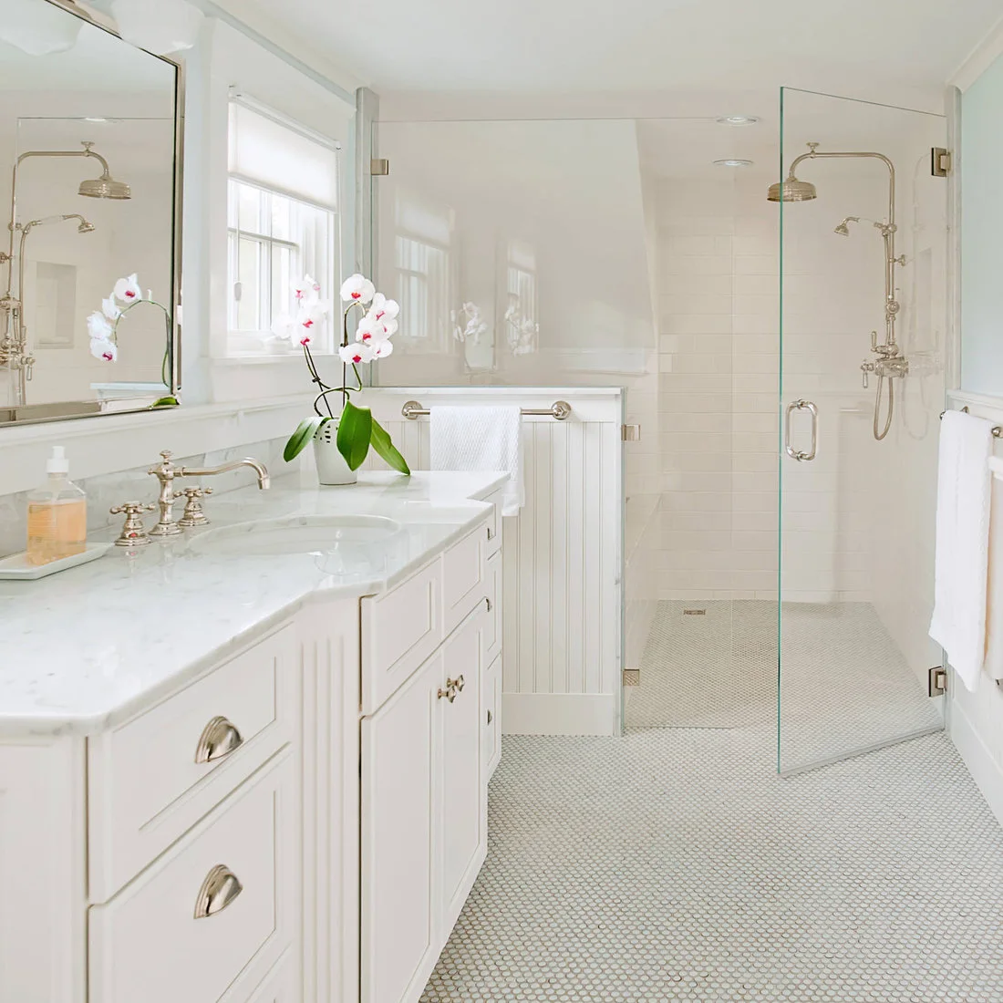 Pale round mosaic floor tiles continue from a white vanity into a glass-enclosed shower.