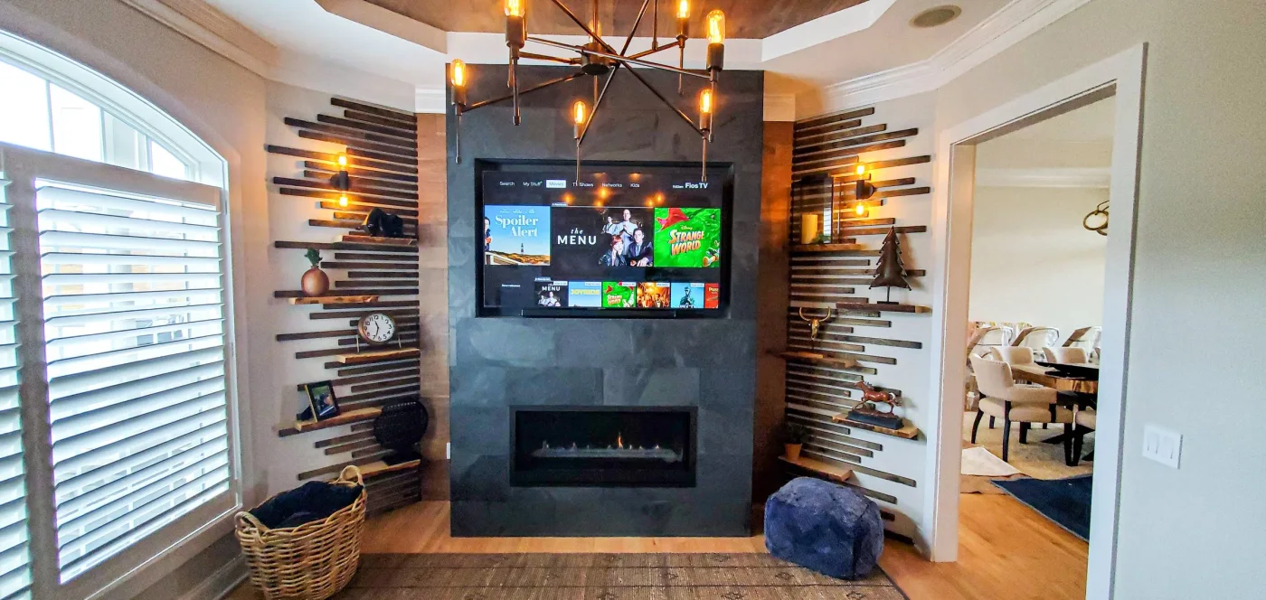 A slate-clad chimney face holds a television and horizontal fireplace between timber slats and staggered shelves.