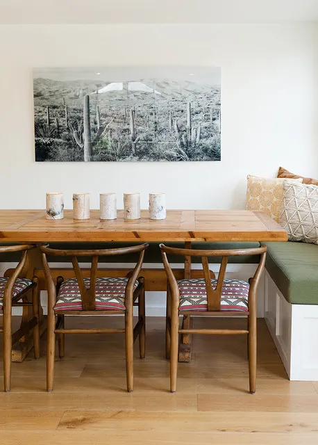 A wooden table and curved wooden chairs sit beside a green cushioned corner bench beneath a wide monochrome photograph