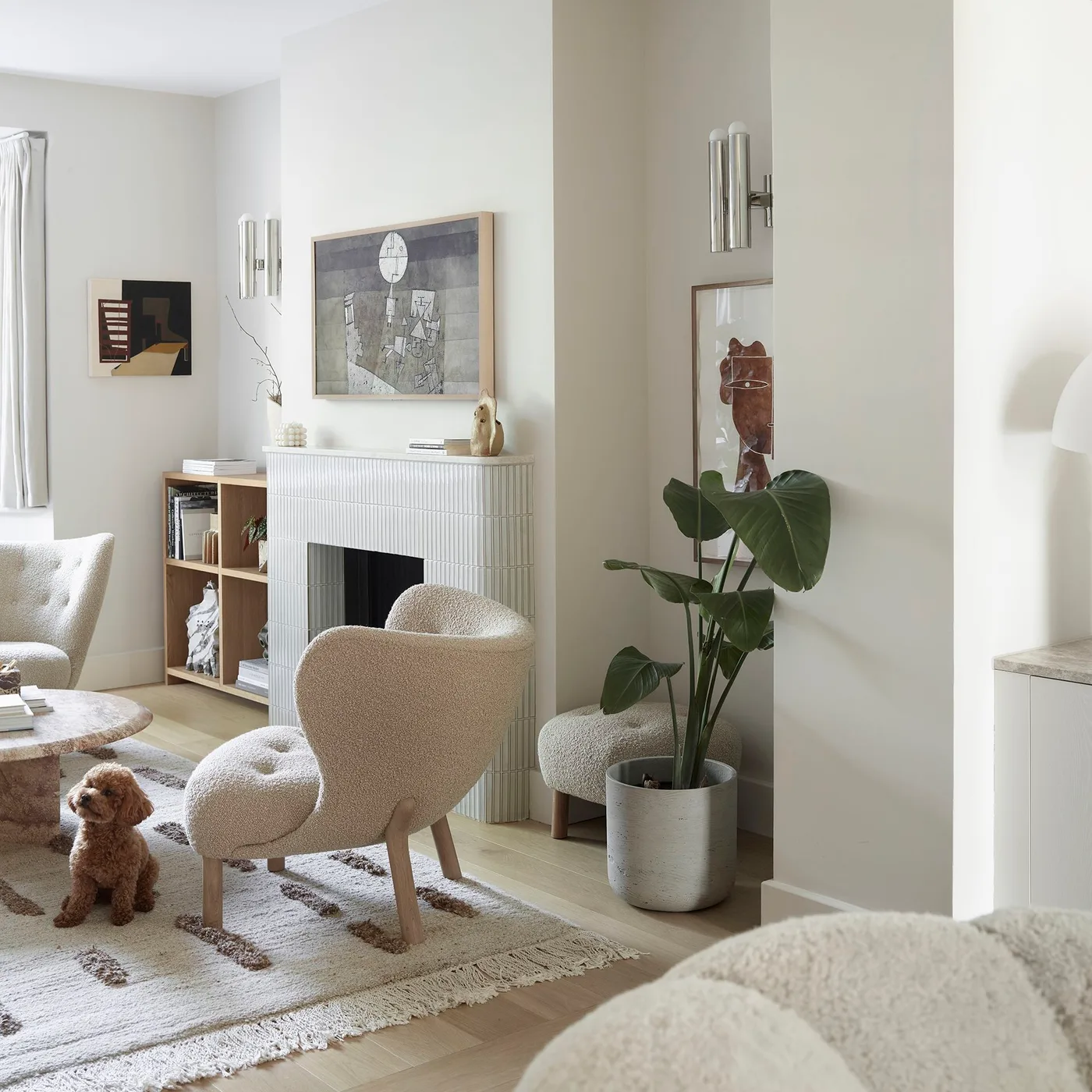 Textured pale armchair beside a light fireplace, wood shelving, a large leafy plant and a pale patterned rug