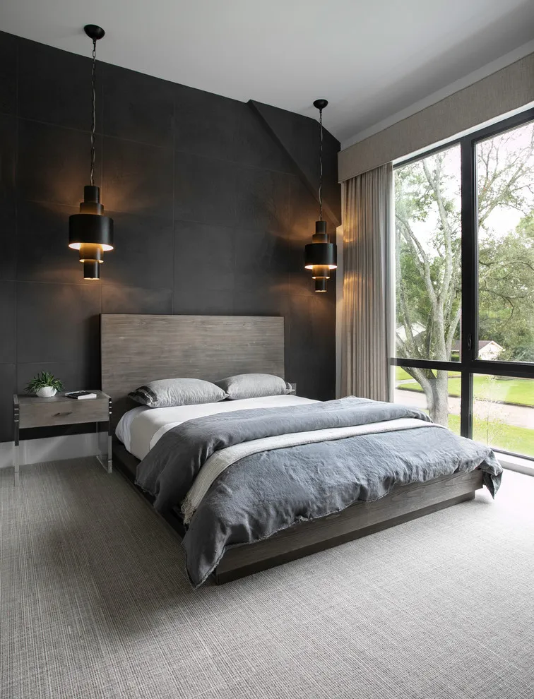 A charcoal wall stands behind a gray bed beside a tall garden-facing window