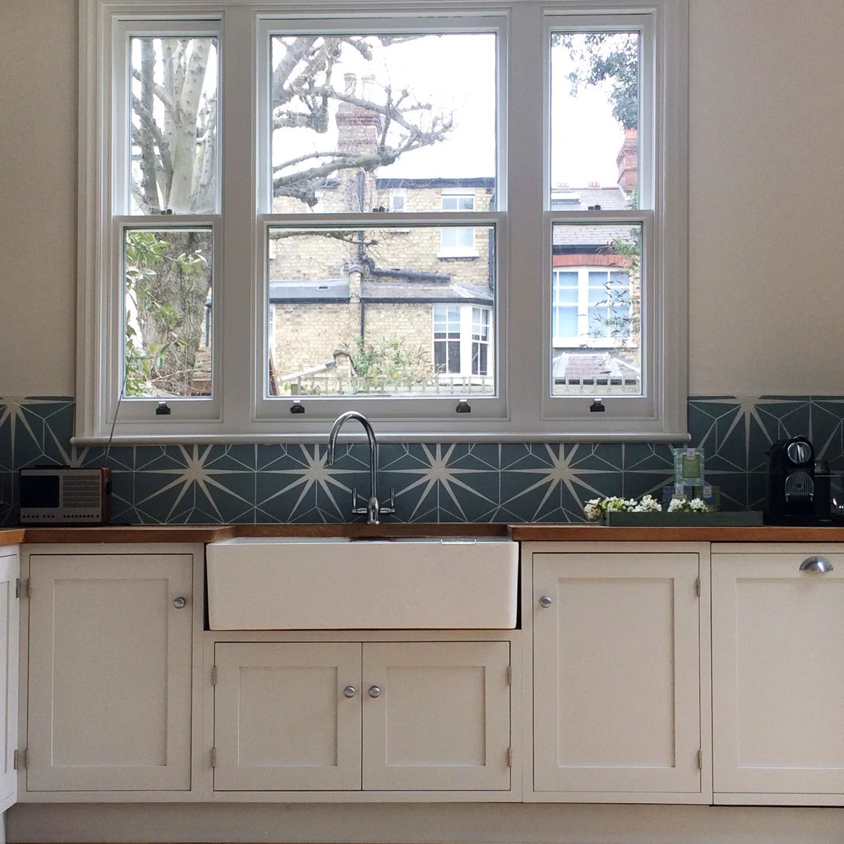 Edwardian terrace kitchen with a pale apron-front sink, tall windows and blue geometric splashback