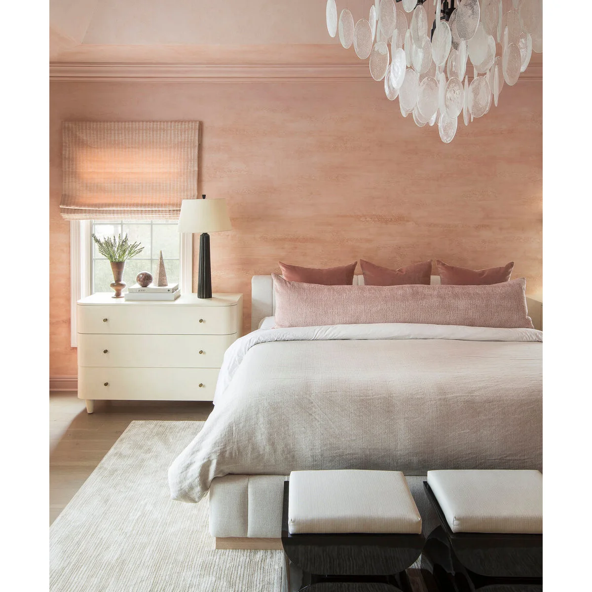 Peach bedroom with a pale upholstered bed, long pink cushion and rounded white bedside chest