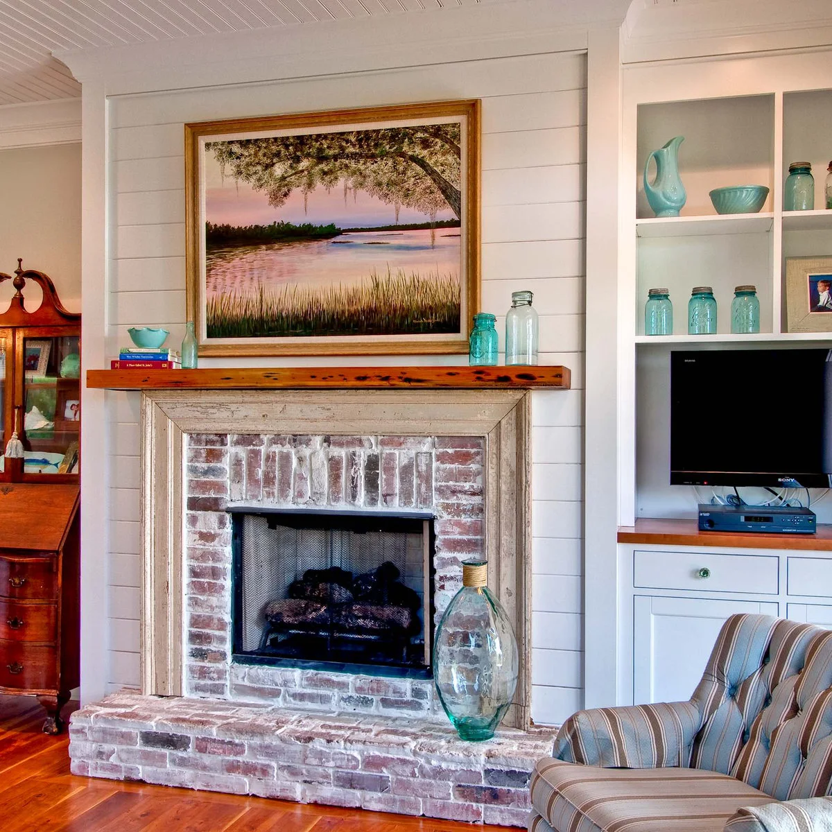 Pale varied brick surrounds a dark fireplace opening beneath a weathered pale frame and wood shelf, with white wall boards behind.