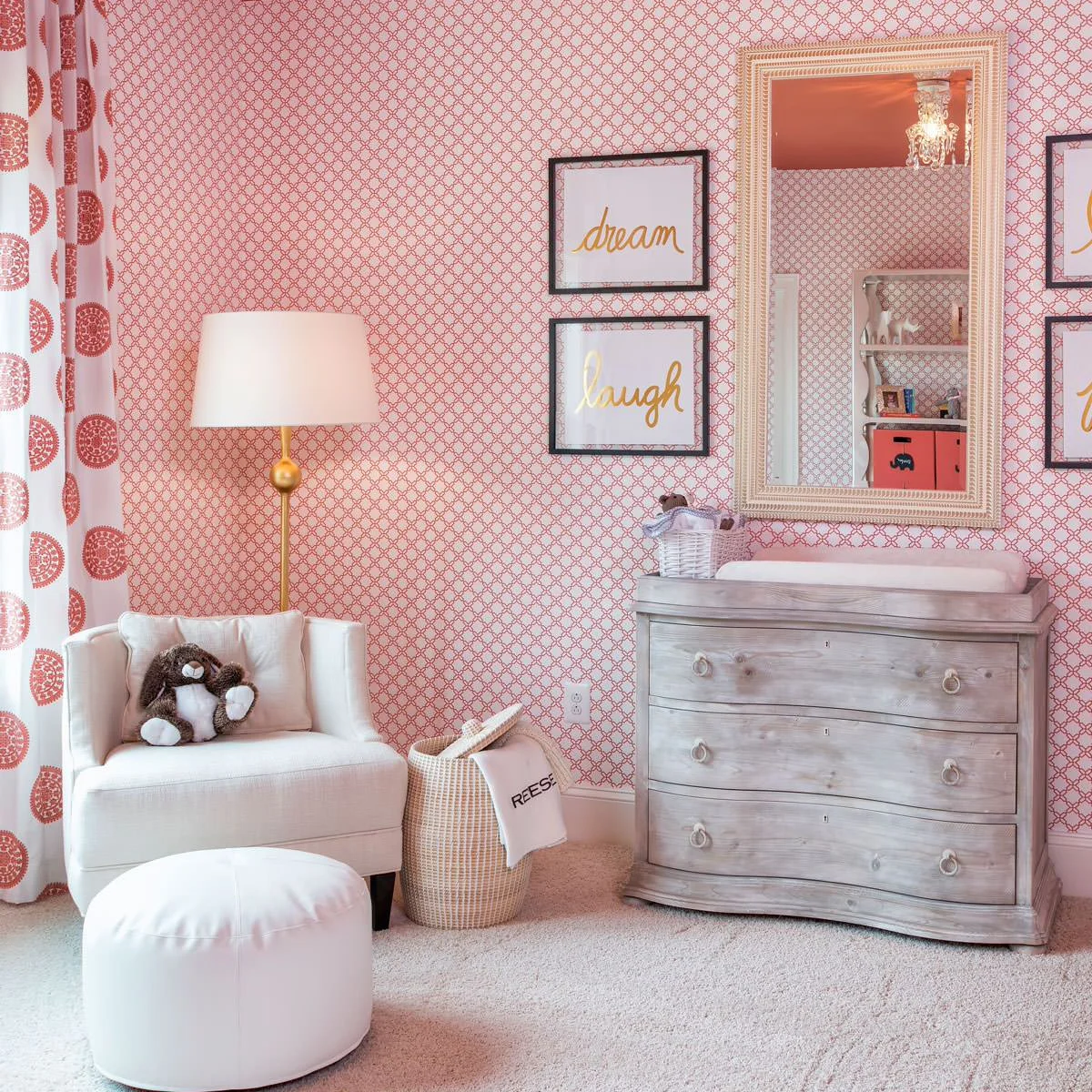 Coral patterned nursery wall behind a grey wood dresser, pale chair and white footstool