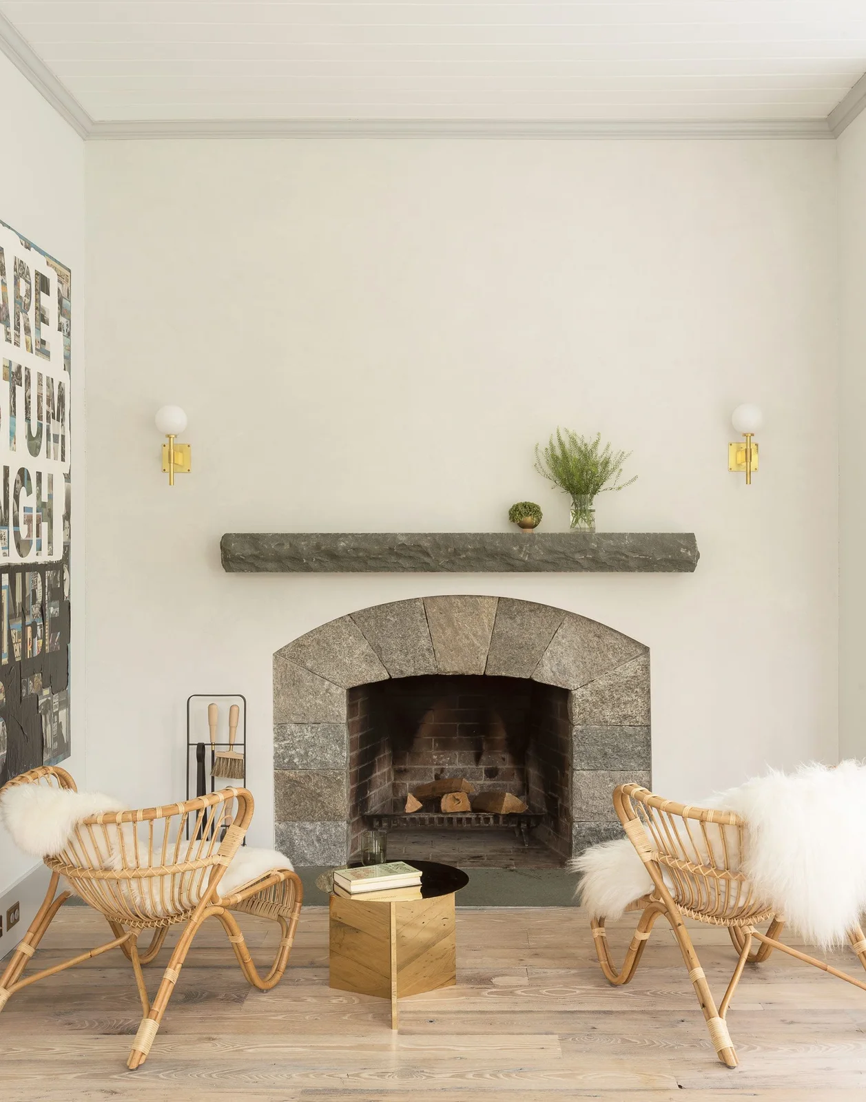 A gray stone arch and rough-edged mantel sit between woven chairs against a pale wall.