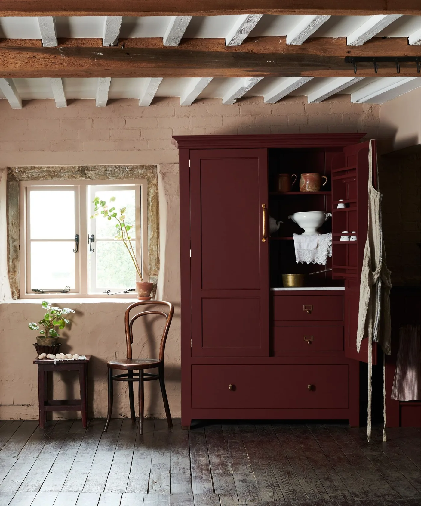 Deep red freestanding country cupboard with open shelving and door rack beneath exposed ceiling beams