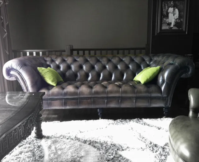 A black tufted leather couch has two bright green cushions against a dark wall above a pale rug