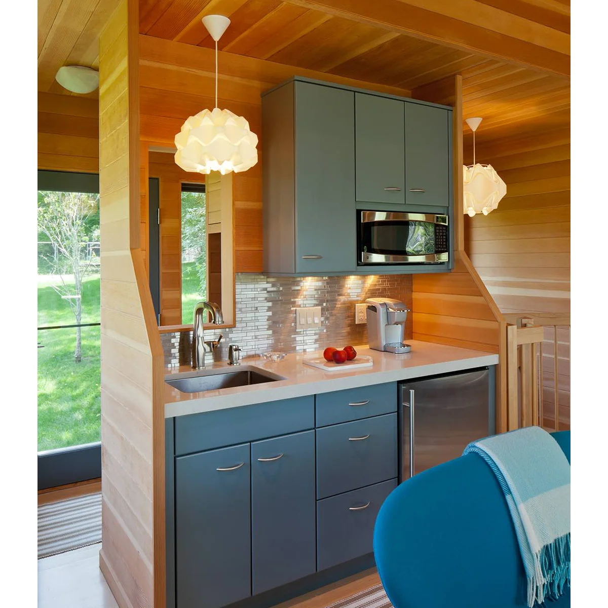Blue-gray kitchenette cabinets with a sink, upper microwave and small stainless refrigerator