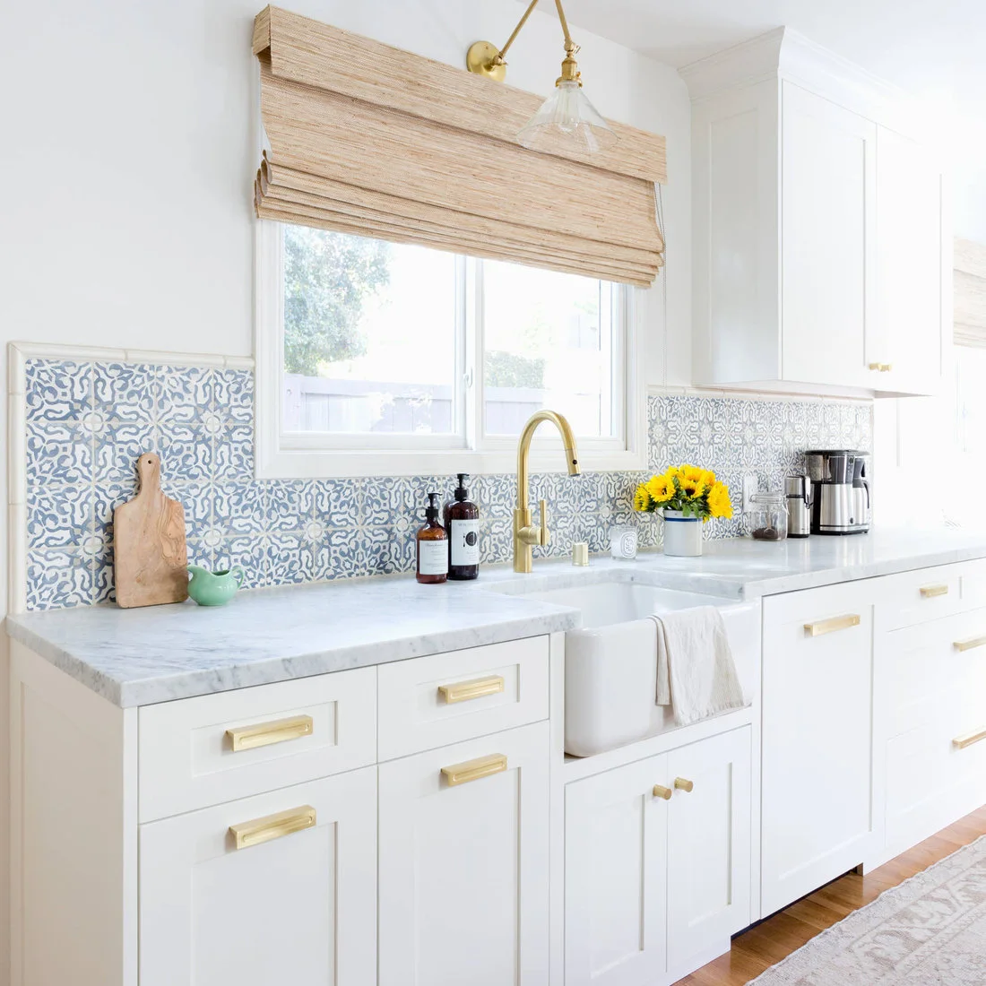 Blue-and-white patterned backsplash tiles run beneath a window above a white apron-front sink and brass-colored fittings.