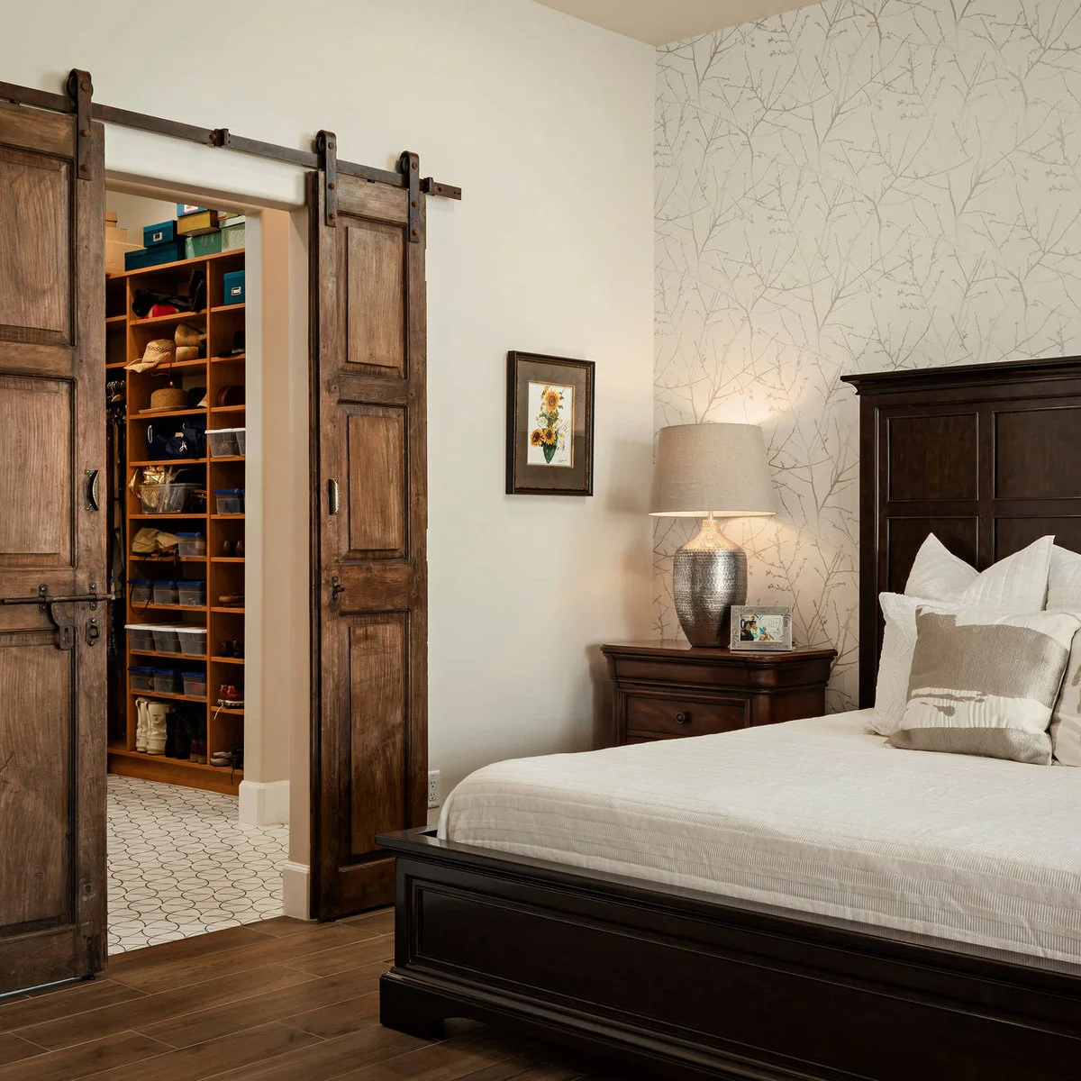 Bedroom with dark wood furniture, a longhorn cushion, branch-pattern wall covering and weathered sliding closet doors