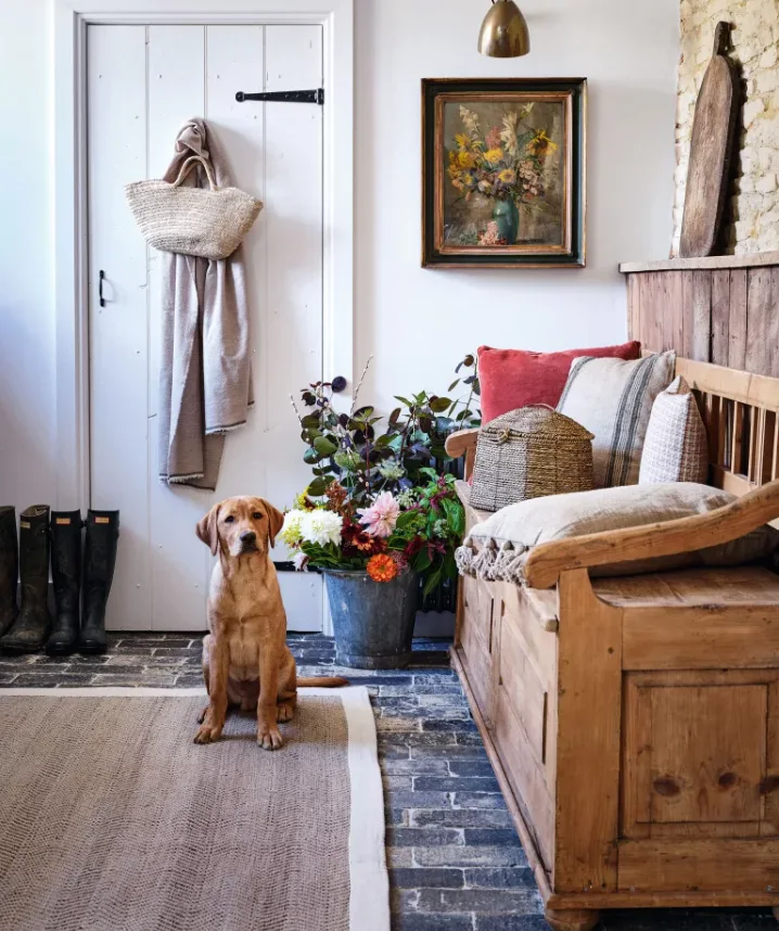 A timber storage bench with red and pale cushions beside a white door in a country hallway
