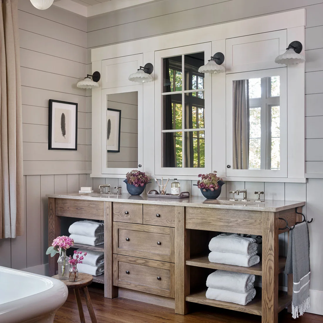 A timber double washstand with open towel shelves beneath mirrors and pale wall boards