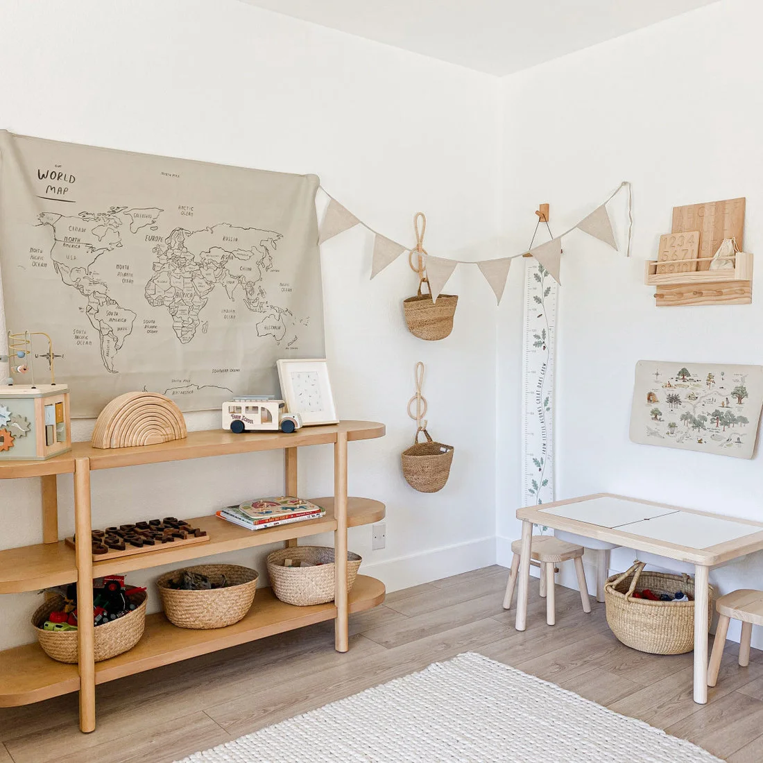 Low pale wood shelves with rounded sides hold woven baskets and wooden toys beside a small child’s table and stools.