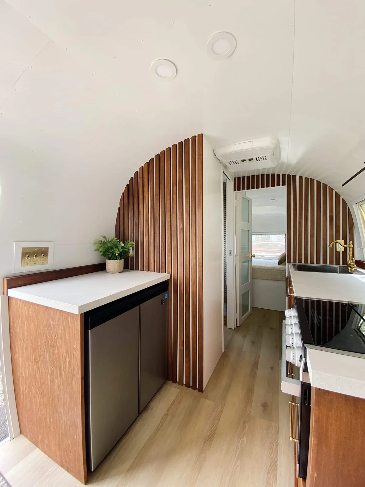 Airstream galley with vertical wood slats around a doorway, a small undercounter refrigerator and pale work surfaces.