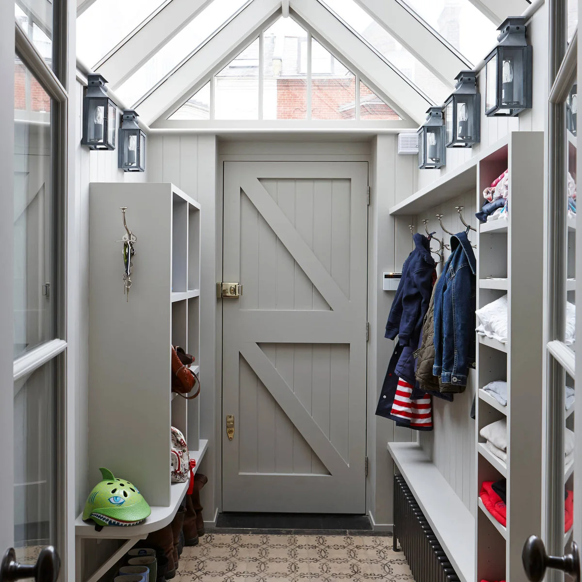 Small glazed-roof entrance porch with gray fitted benches, cubbies, coat hooks and a paneled exterior door.