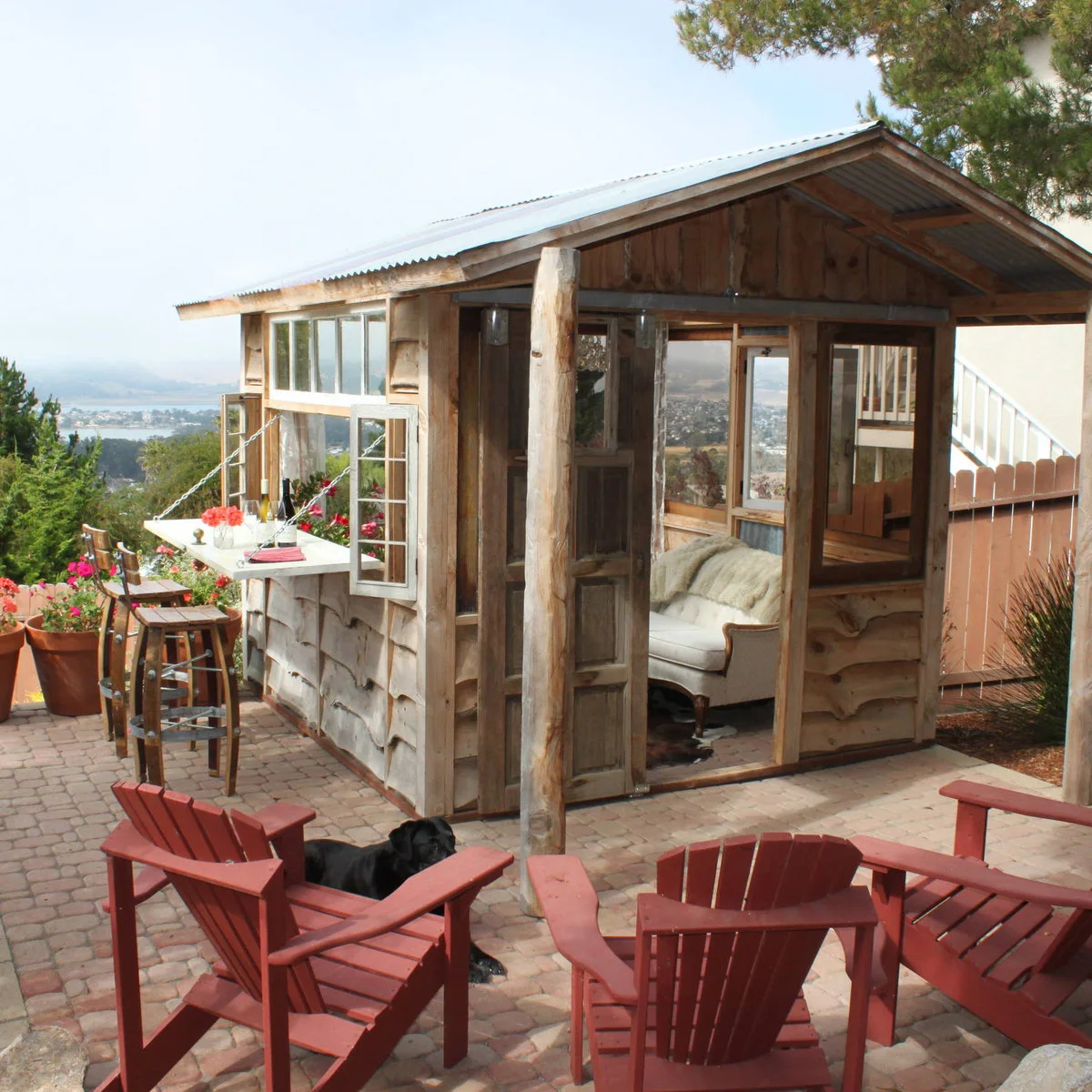 Rustic wood shed with a fold-down serving ledge, tall stools and outdoor chairs