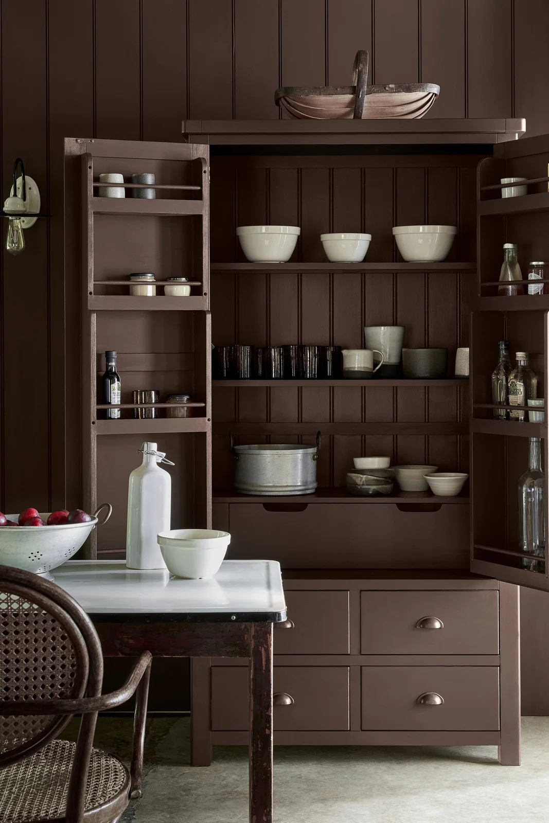 Brown cupboard with bowls, mugs and glasses on separate shelves and racks inside doors