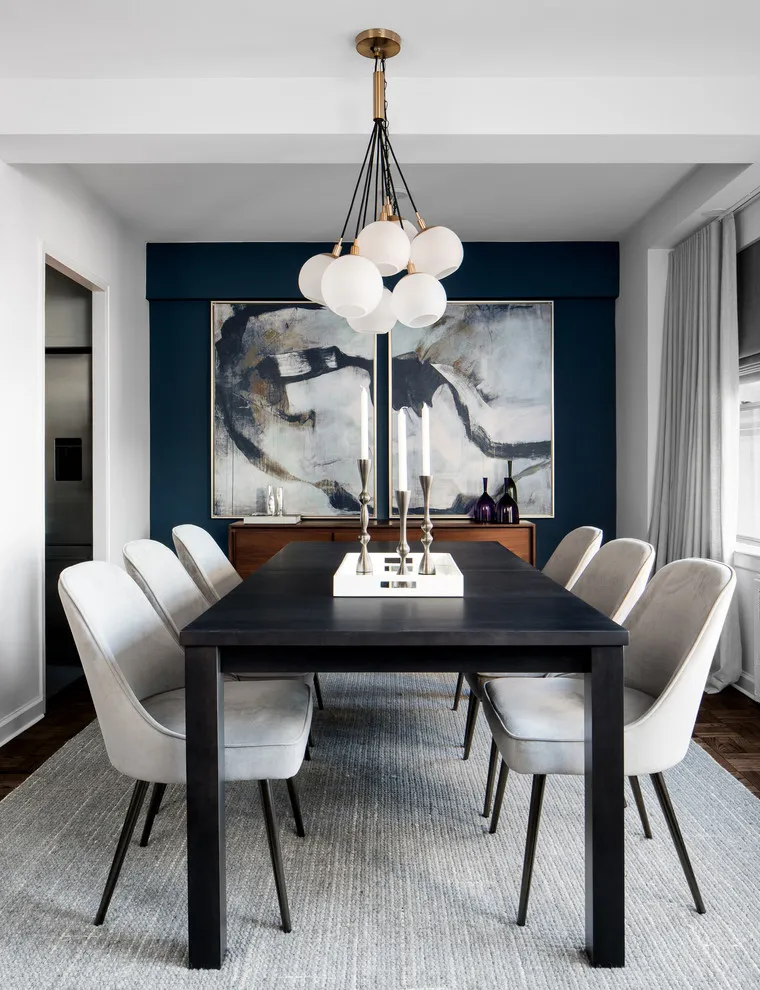 A dark dining table and pale chairs sit beneath a globe light against a deep blue wall