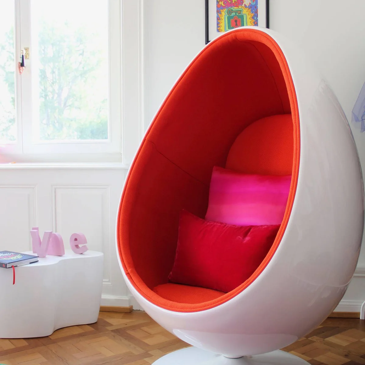 White pod chair with an orange interior and pink cushions beside a teen bedroom window