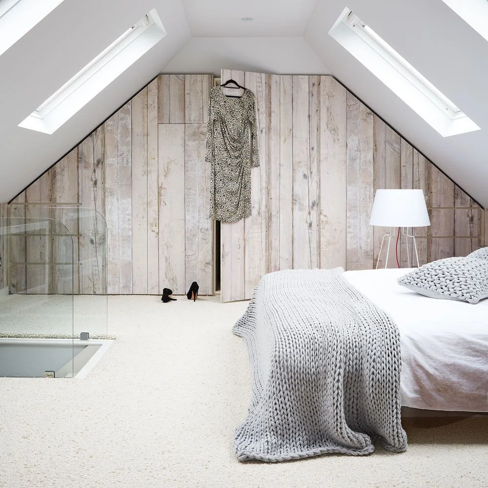 Pale wood-effect wardrobe fronts fitted to an attic gable with roof windows on both slopes and a bed in the foreground.