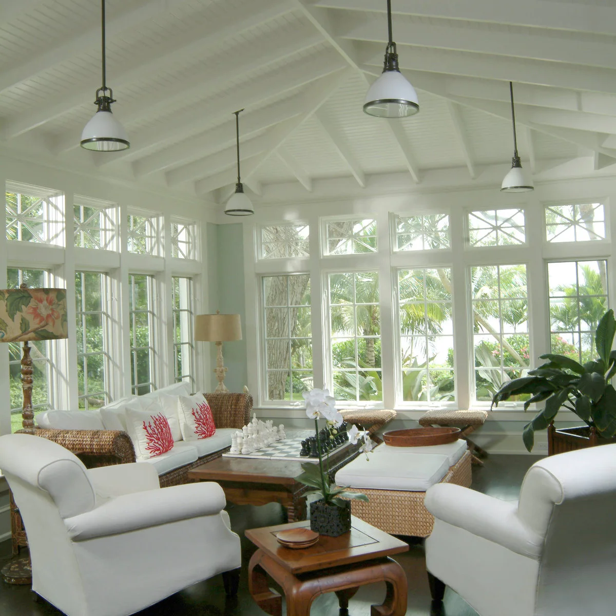 A bright sunroom with white seating, woven furniture and a chessboard on the central coffee table.