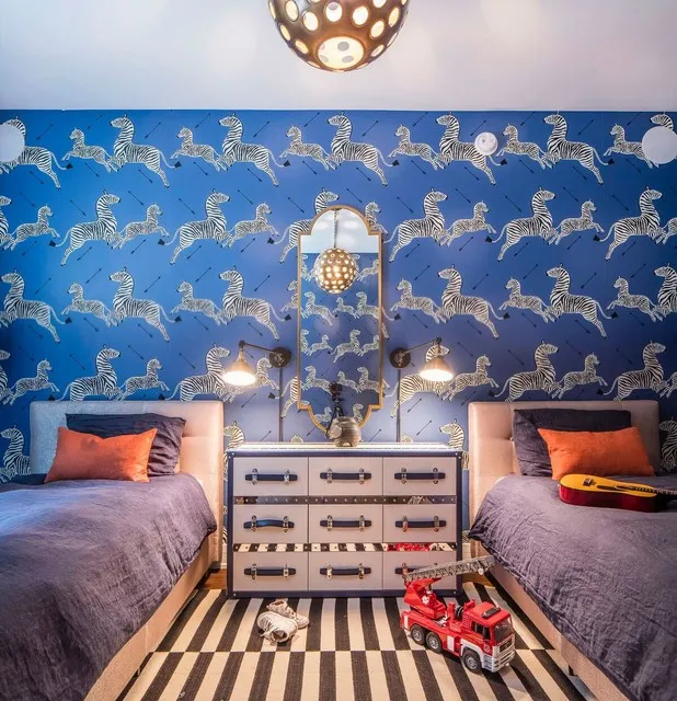 A vivid blue illustrated wallpaper surrounds two beds and a pale central chest.