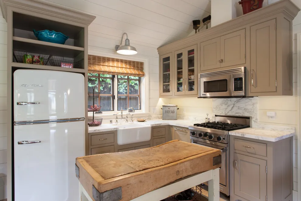 Beige cabinetry surrounds a compact kitchen with a wooden worktable in the center