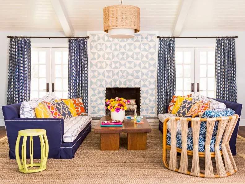 Pale blue and white geometric fireplace wall between two windows with blue curtains and colorful seating