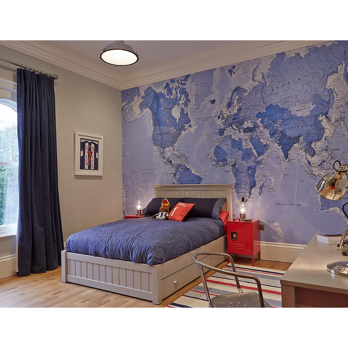 Boy’s bedroom with a blue world-map wall, pale bed frame and red locker-style bedside units