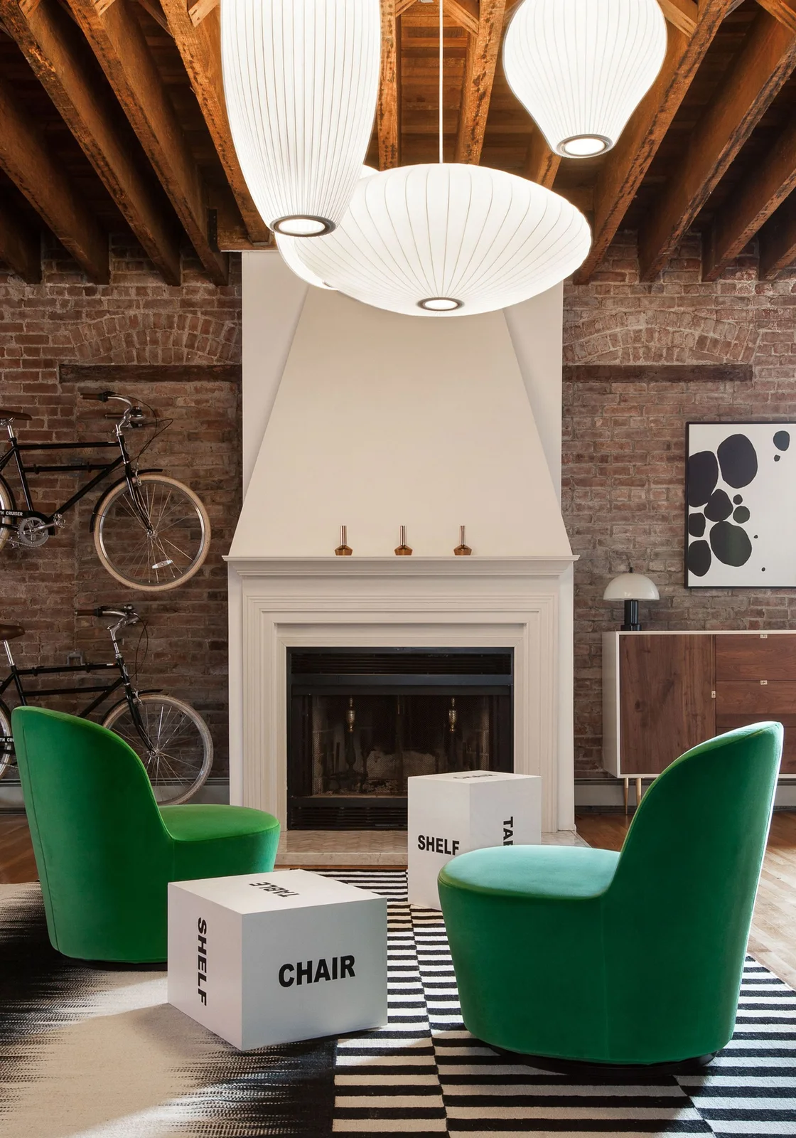 White ribbed pendant lights above green chairs beside a brick fireplace wall and mounted bicycles