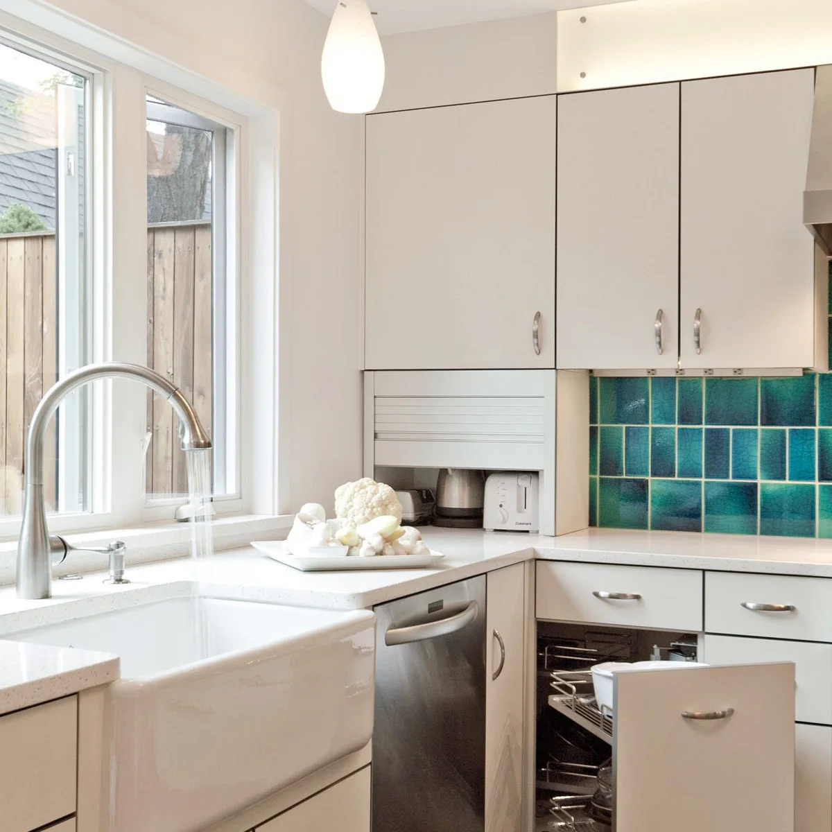 White kitchen corner with a roller-front appliance cupboard above an open base pull-out