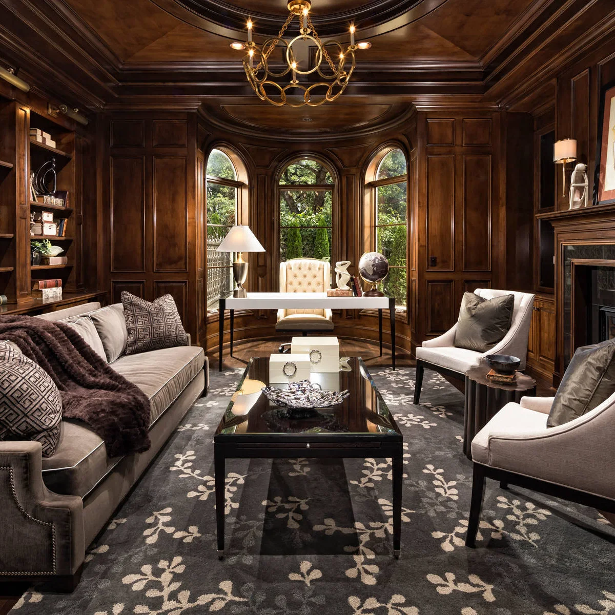 A pale desk in a wood-paneled bay behind a sofa and two armchairs grouped around a coffee table.