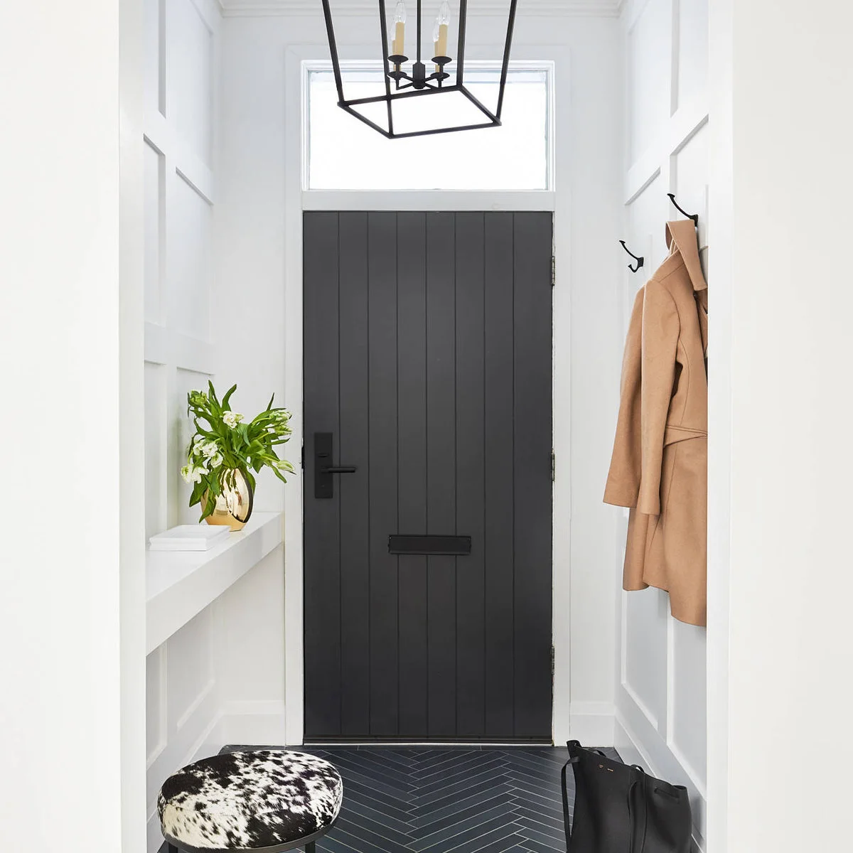 Small white paneled entrance with a dark front door, shallow wall ledge, hooks and a black floor.
