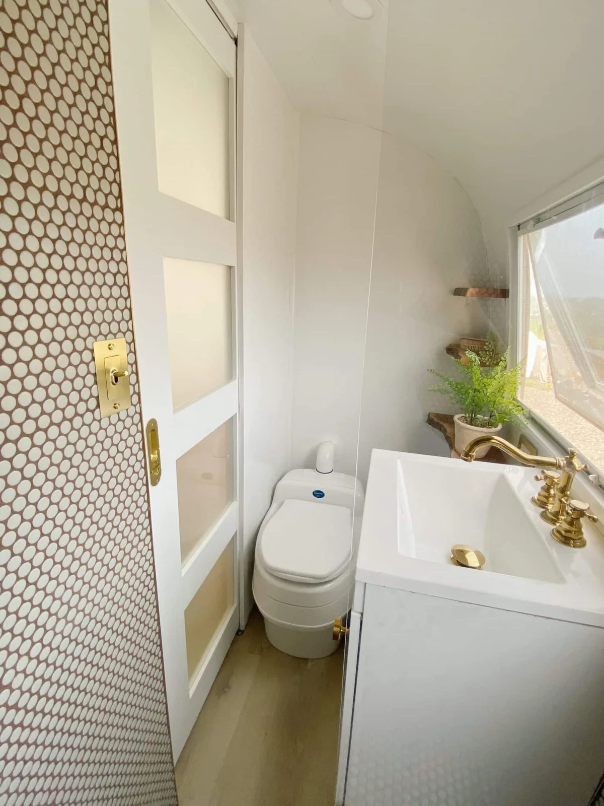 Compact Airstream bathroom with a sliding white door, small basin, gold-colored tap and curved white wall.