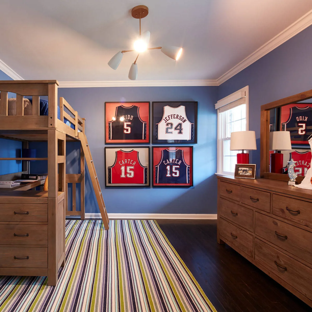 Blue boy’s room with four framed basketball jerseys beside wood-colored furniture and a striped rug