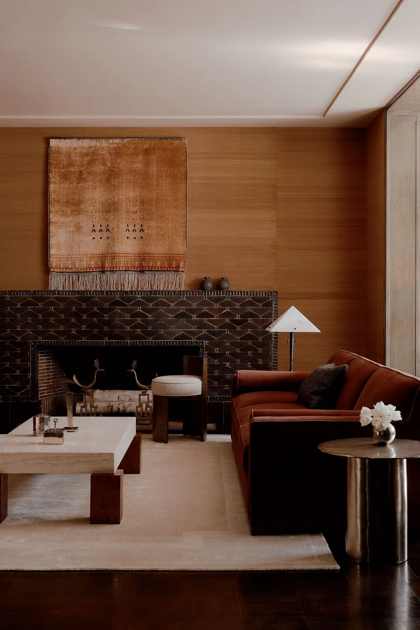 Warm wood-toned living room wall around a dark patterned fireplace, rust armchair and woven wall hanging