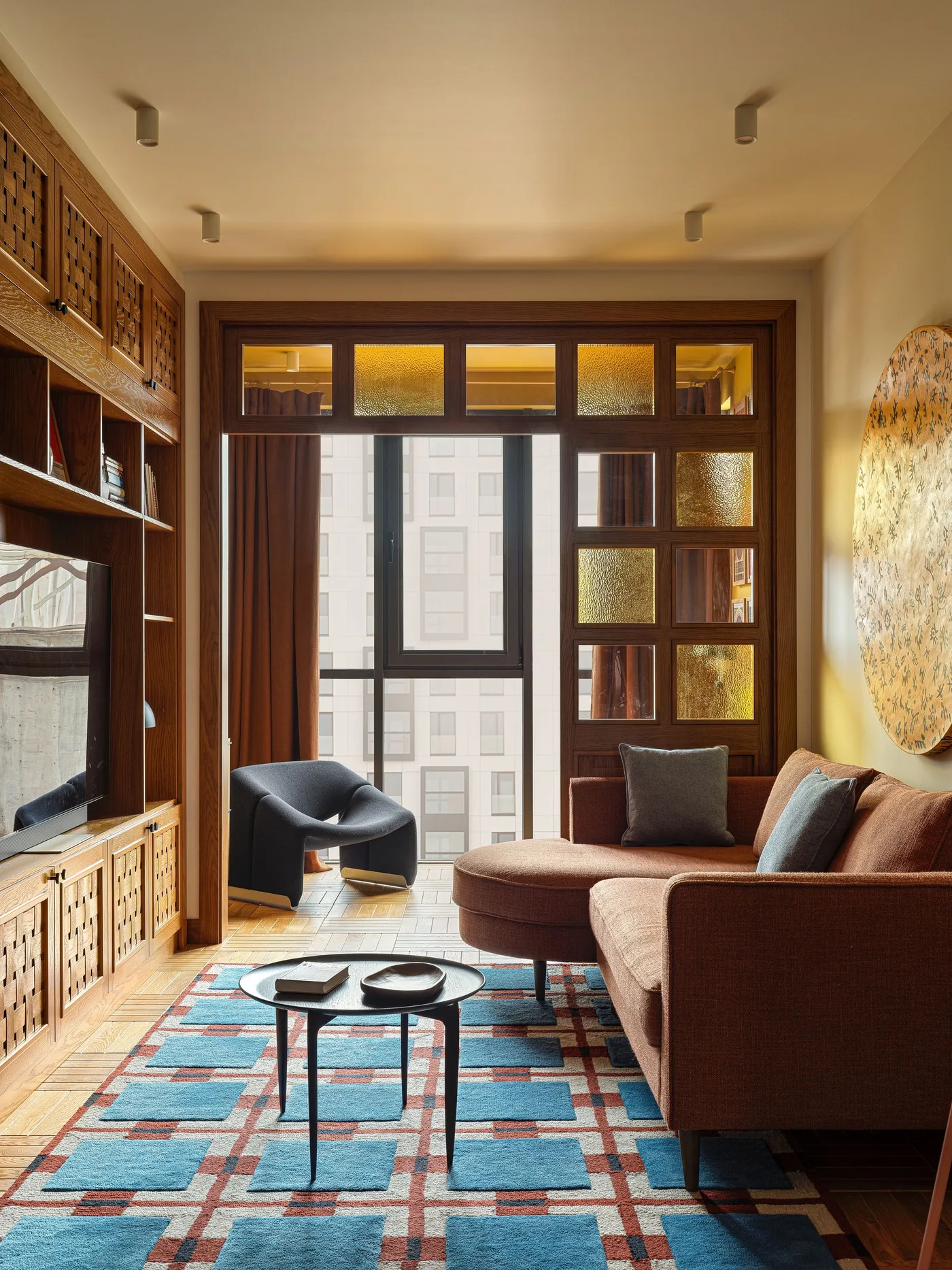 Brown fabric chaise sofa with a turquoise geometric rug beside a wood lattice and glass partition.