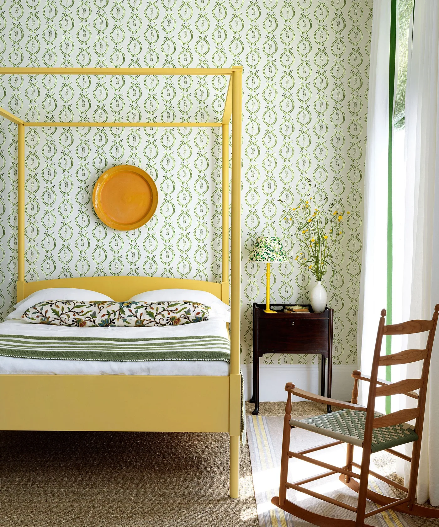 Green-and-white repeating leaf wallpaper behind a yellow four-poster bed with green striped bedding.