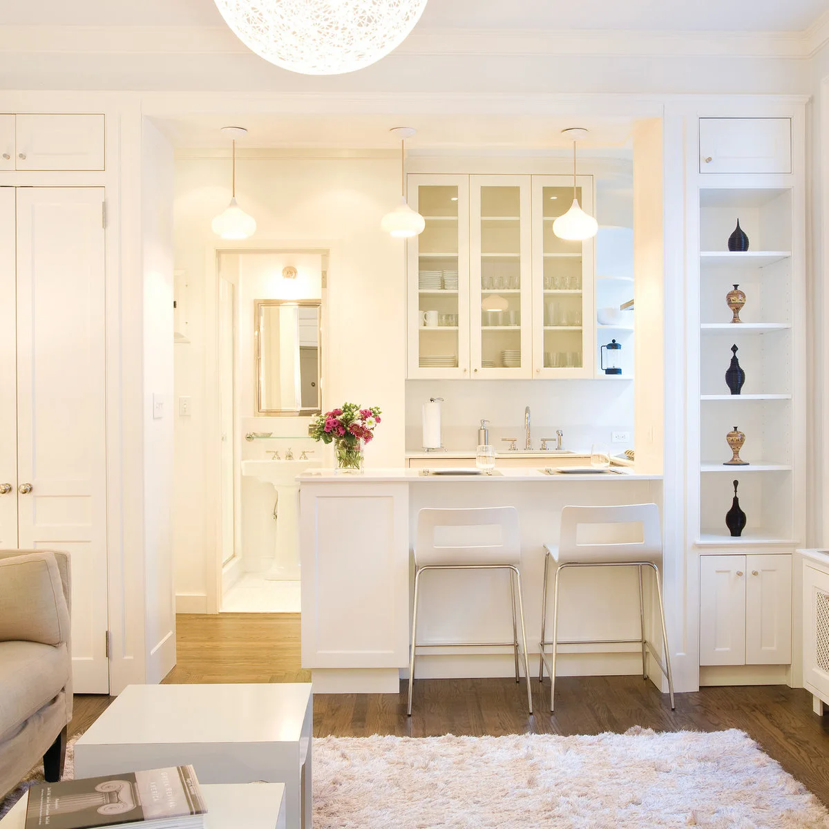 White apartment kitchen seen through a wide opening with two stools at a breakfast bar