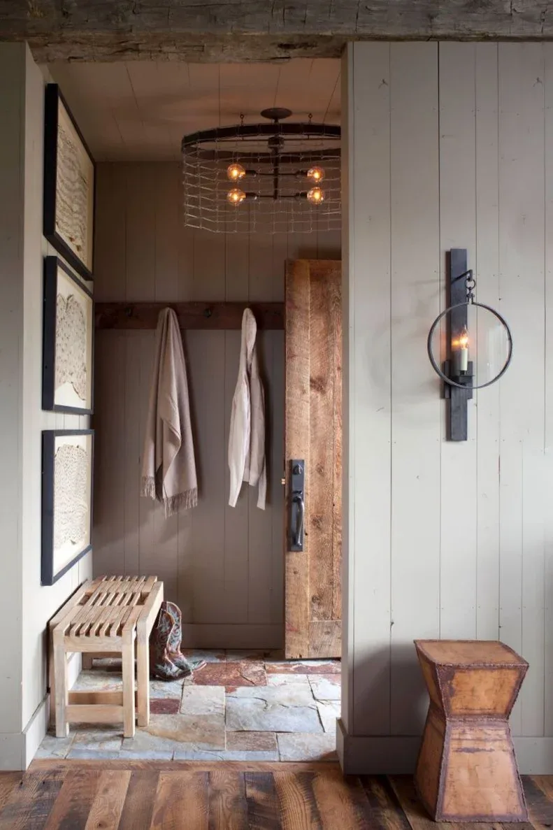 Small rustic vestibule with gray vertical boards, slatted bench, wood sliding door and dark lantern