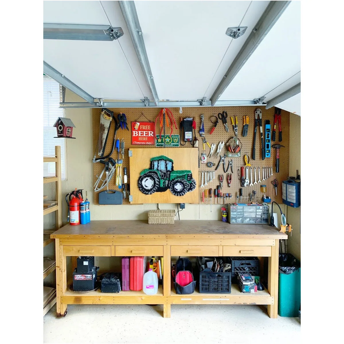 Wooden garage workbench with drawers, open lower storage and a tool pegboard beneath an open overhead door.