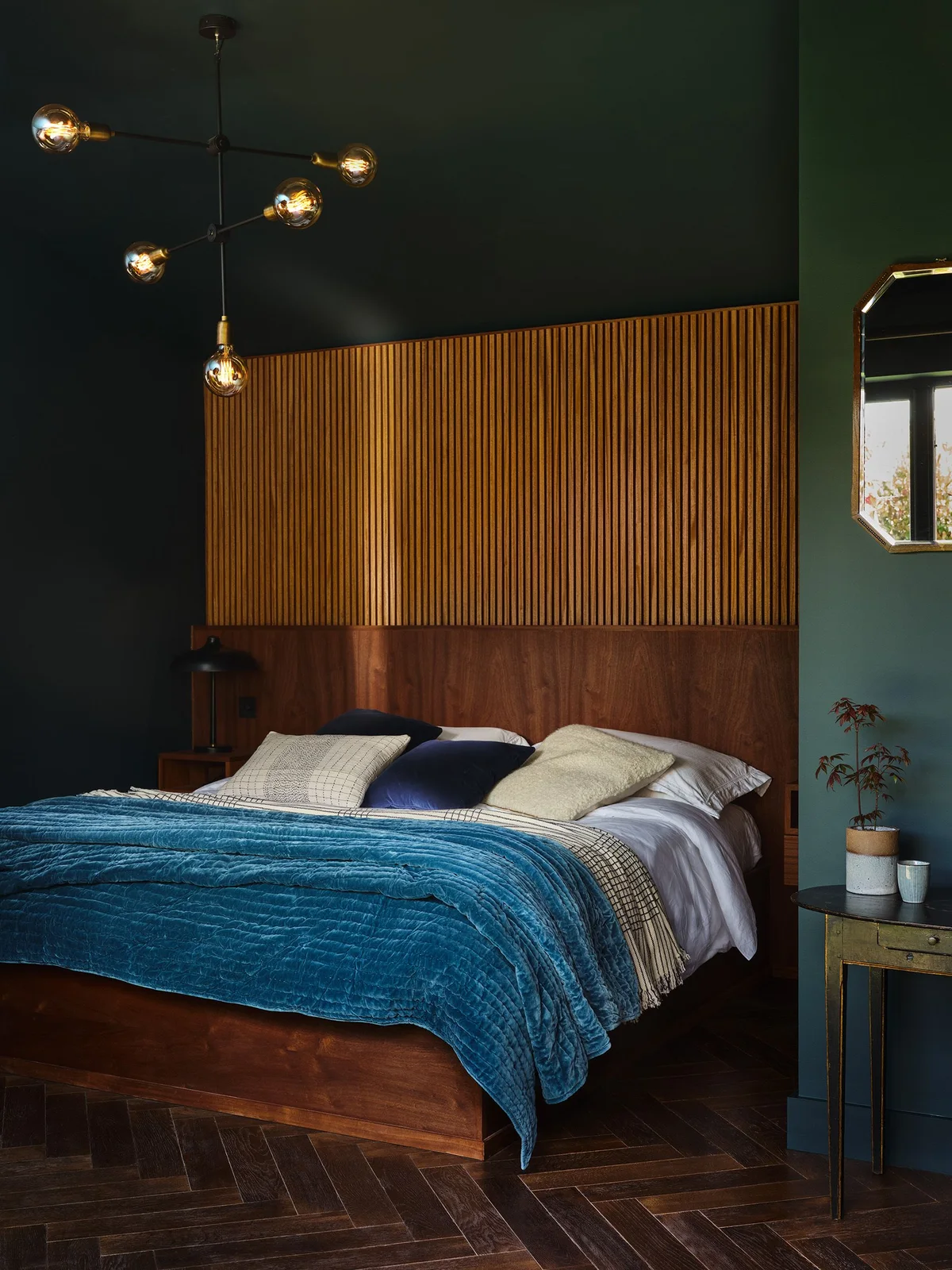 Broad brown headboard beneath vertical wooden slats with dark green walls and a blue quilt.