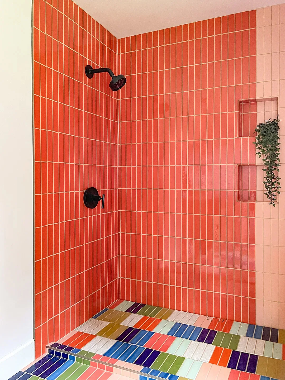 Coral vertical shower tiles surround dark shower fittings beside recessed storage niches and a floor of differently colored rectangular tiles