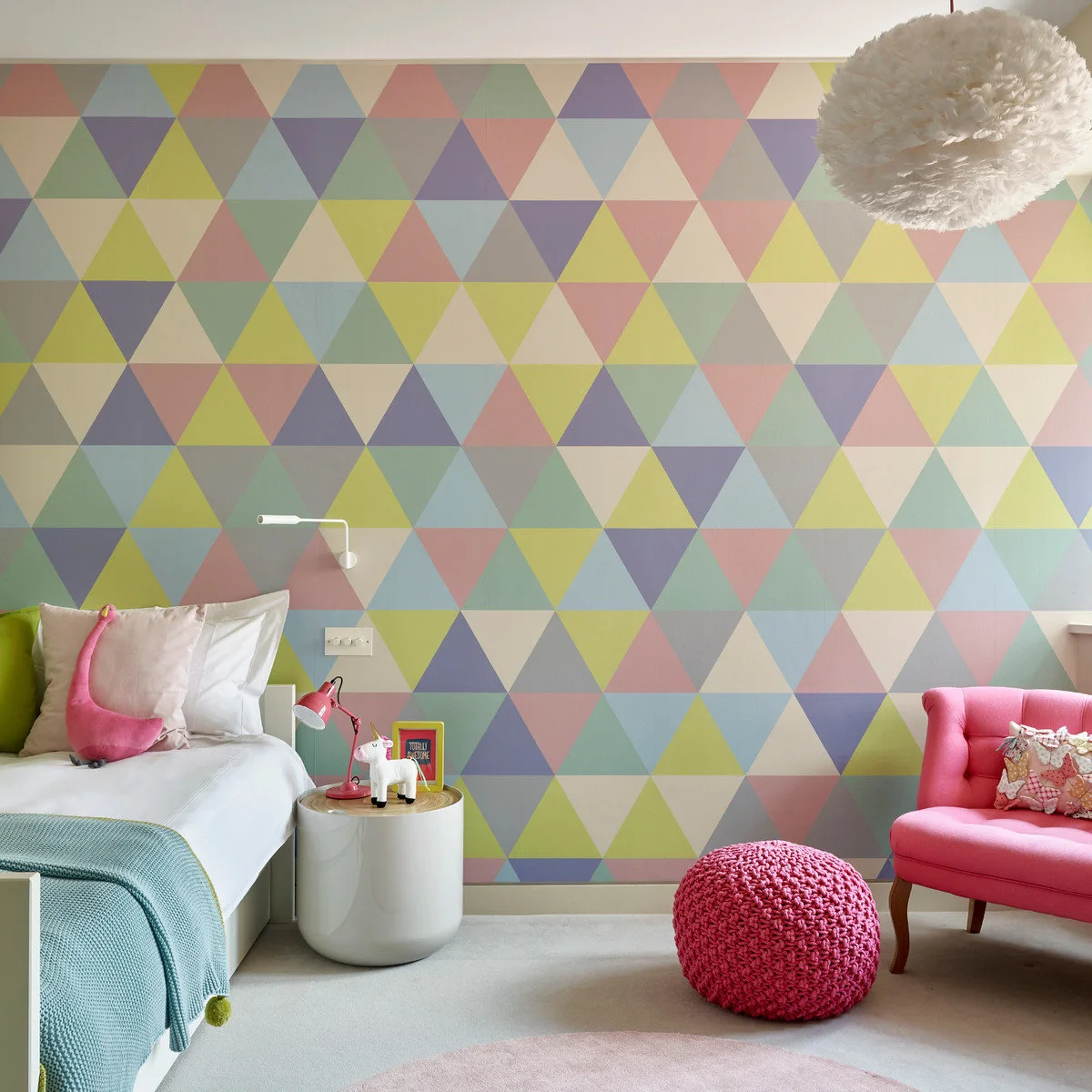 Bedroom with a pastel geometric wall, white bed, teal throw, pink chair and pink pouf