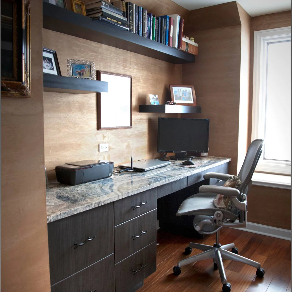 Dark fitted desk with a pale patterned top, printer on the left and monitor near the window