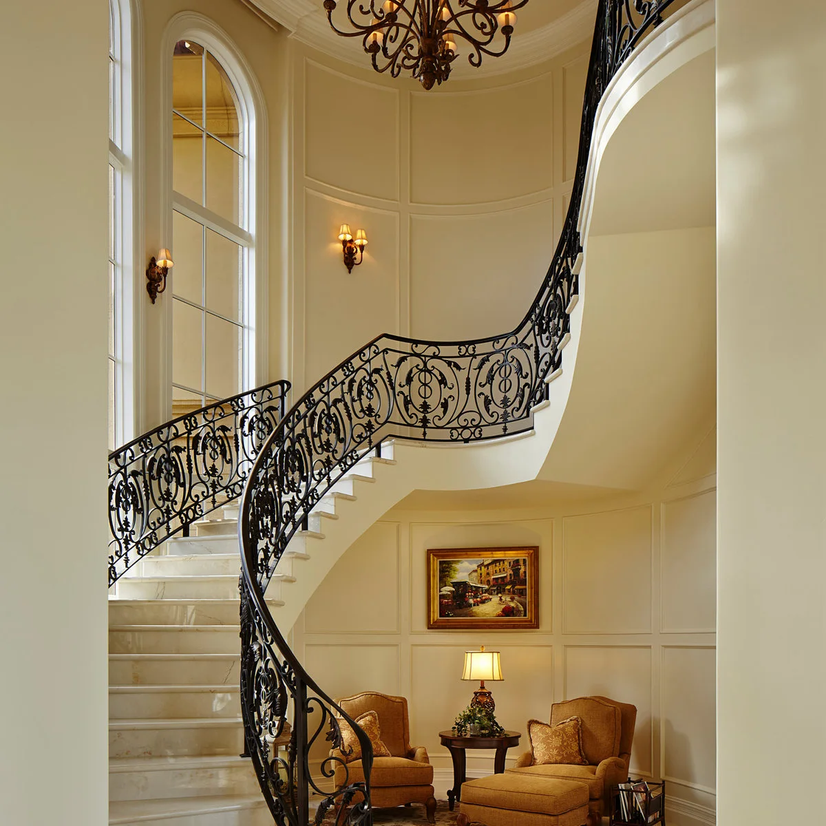 Pale rectangular wall moldings wrap a curved staircase with an ornate dark metal railing.