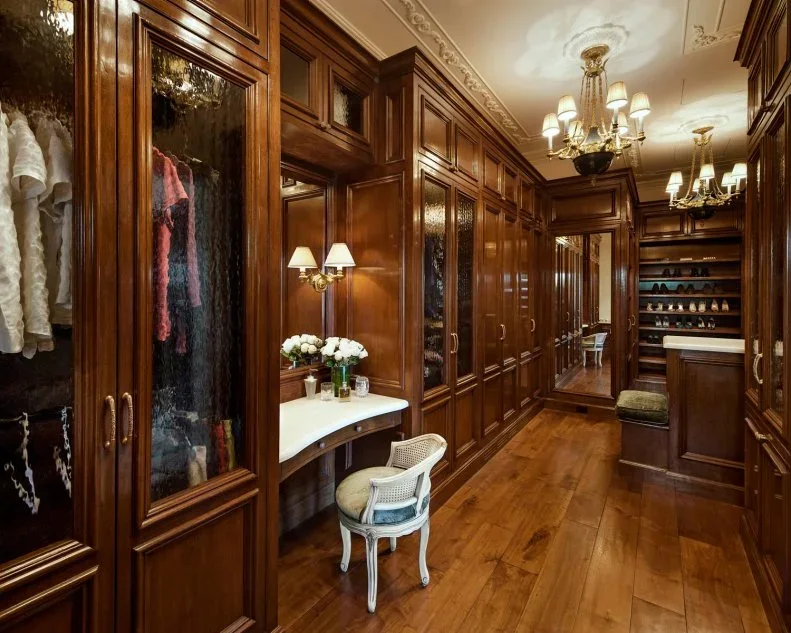 Warm timber closet cabinets with glass doors surround a small dressing table and upholstered chair.