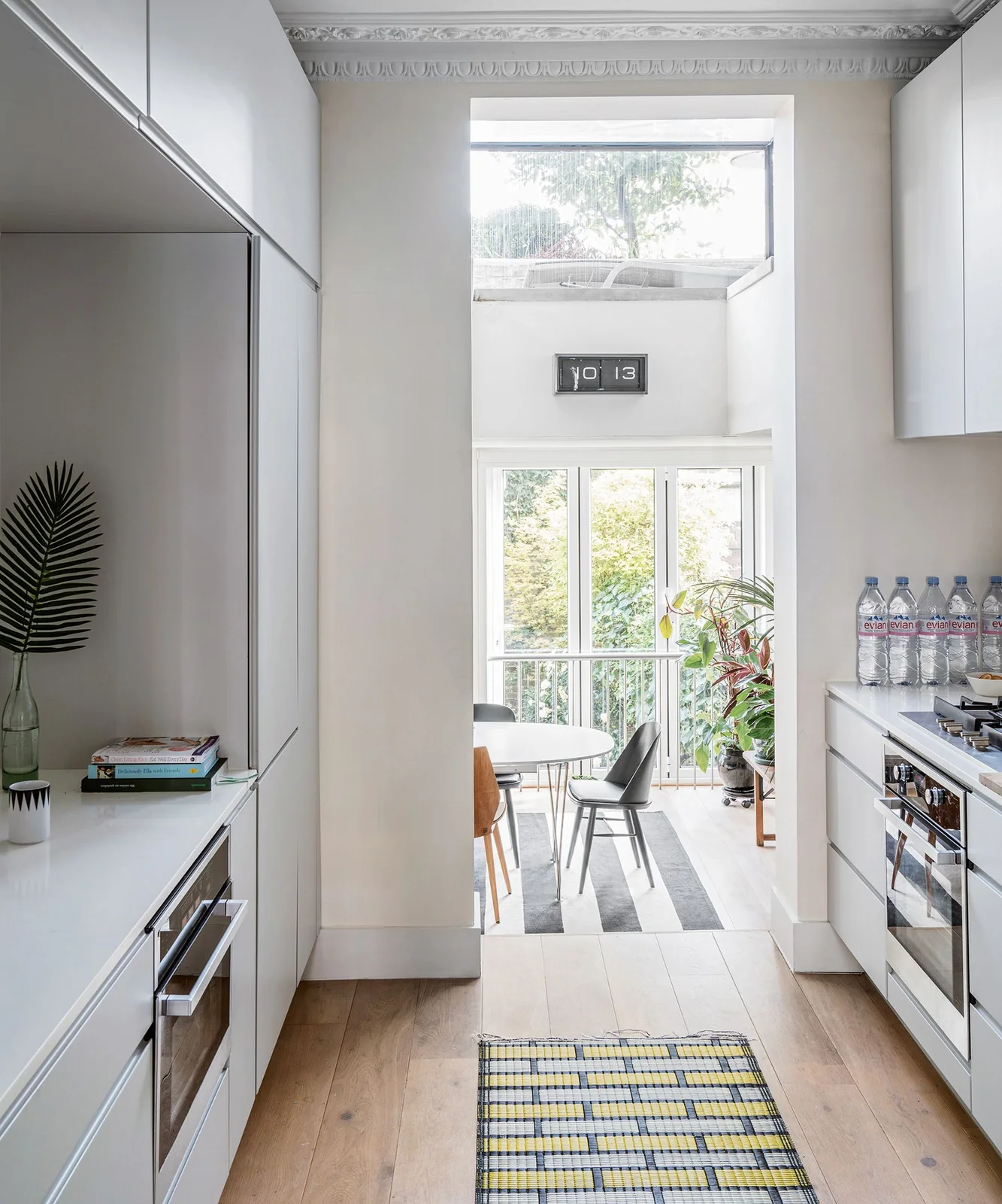 White handleless galley kitchen opening to a bright dining space with large windows